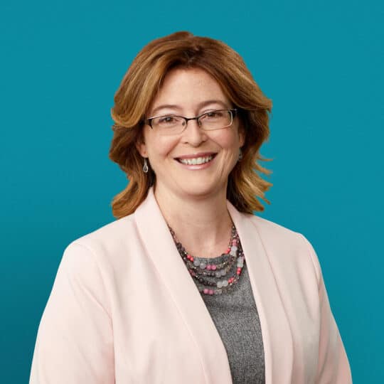 Professional headshot of Dr. Deanna M. Allgeyer smiling in white blazer against teal background