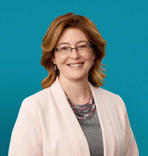 Professional headshot of Dr. Deanna M. Allgeyer smiling in white blazer against teal background