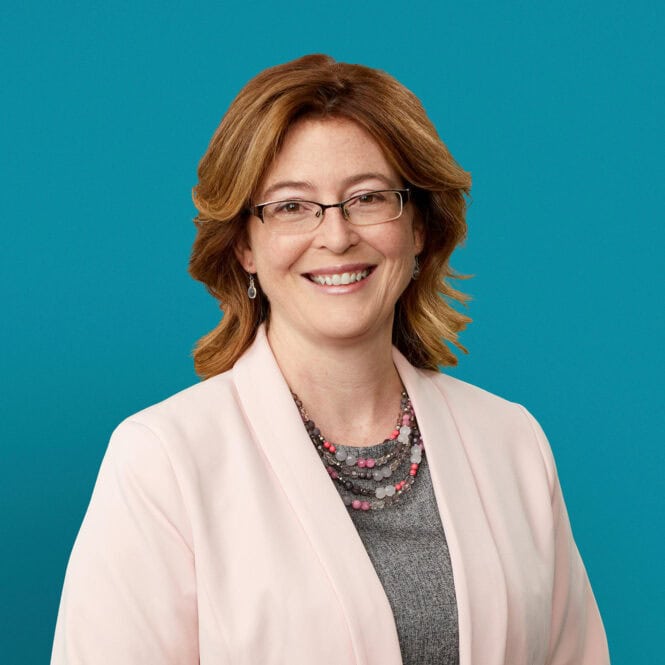 Professional headshot of Dr. Deanna M. Allgeyer smiling in white blazer against teal background