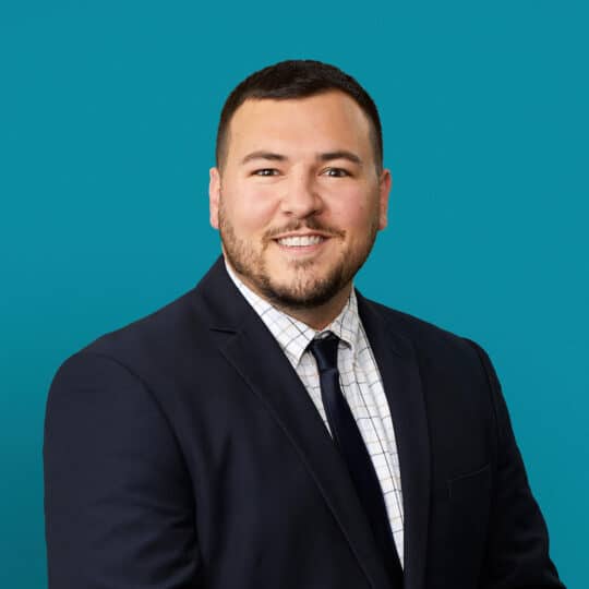 Professional headshot of Drew Guisinger, APRN-CNP in dark suit against teal background