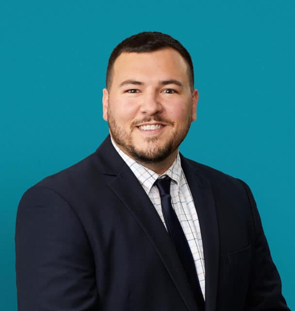 Professional headshot of Drew Guisinger, APRN-CNP in dark suit against teal background
