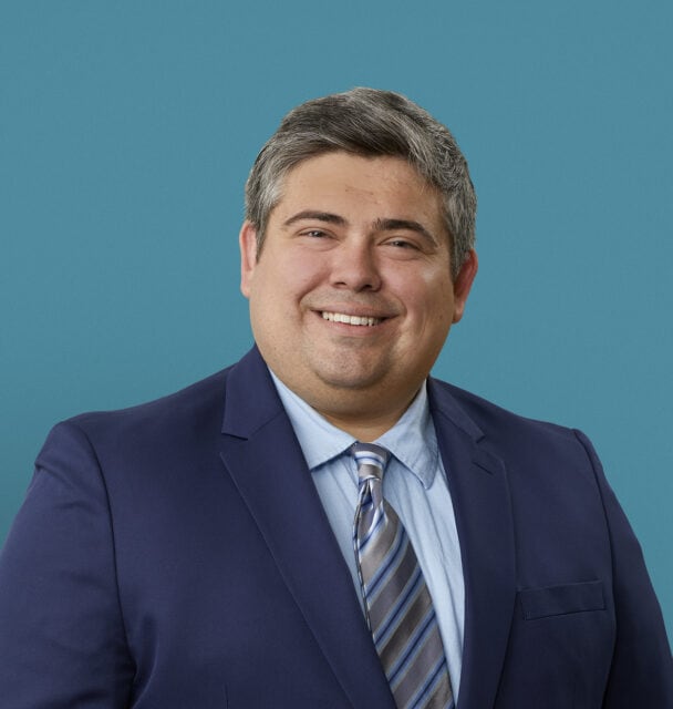 Professional headshot of Dr. Elijah Kelley in navy suit with striped tie