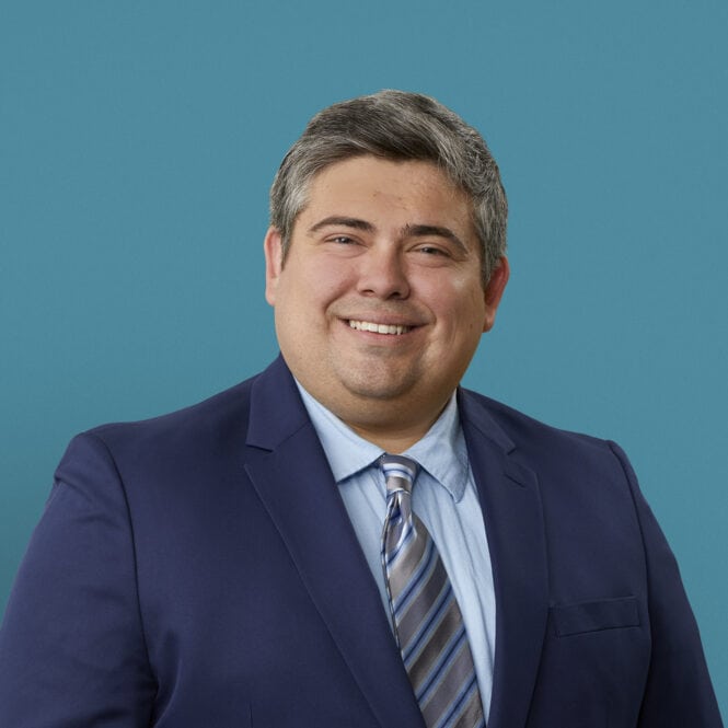Professional headshot of Dr. Elijah Kelley in navy suit with striped tie