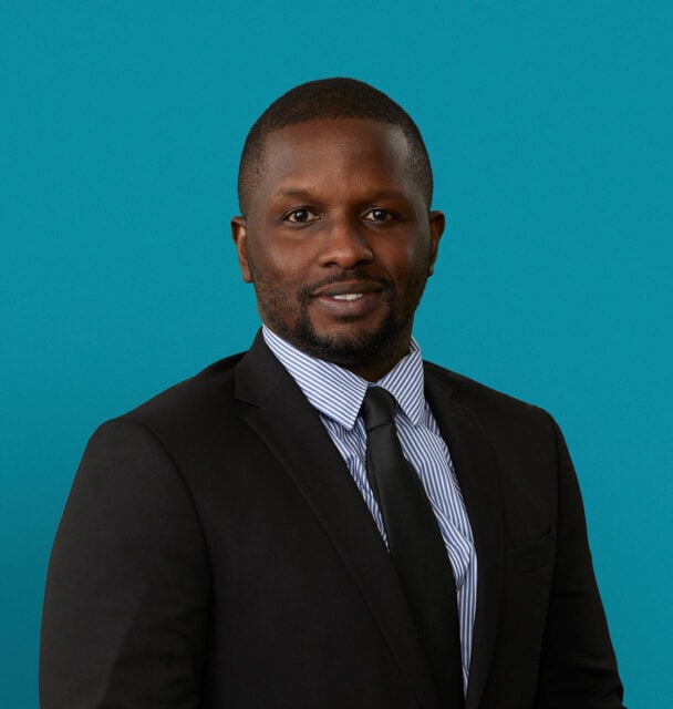 Professional headshot of Emmanuel Aguh, MD in dark suit against teal background