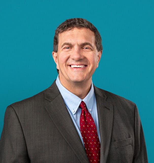 Professional headshot of Dr. Fredrick M. Reeve in gray suit with red tie