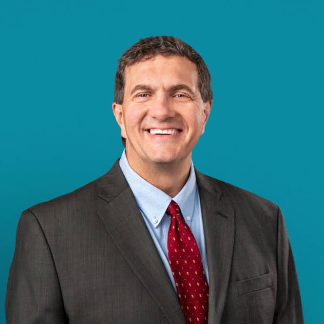 Professional headshot of Dr. Fredrick M. Reeve in gray suit with red tie
