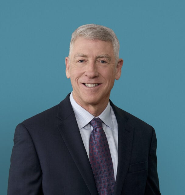 Professional headshot of Gregory Haack, MD smiling in dark suit against blue background