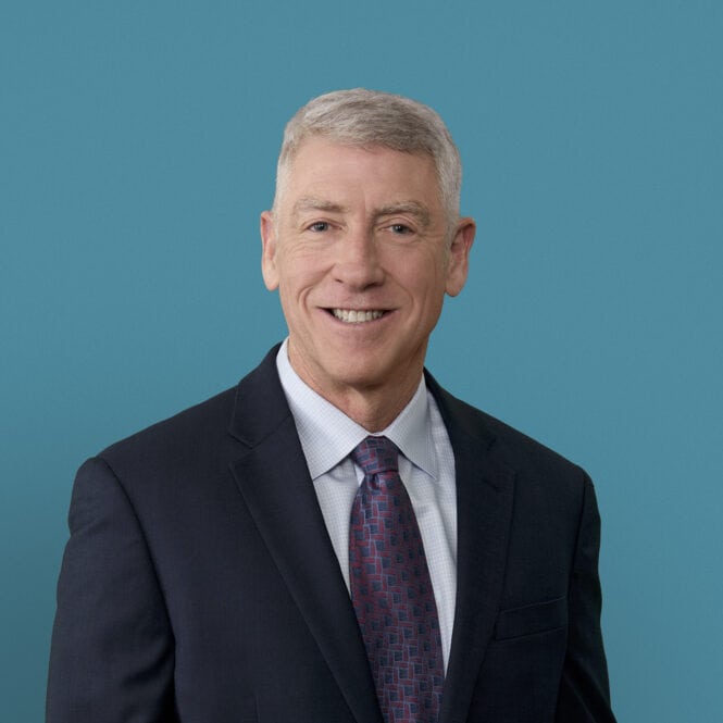 Professional headshot of Gregory Haack, MD smiling in dark suit against blue background