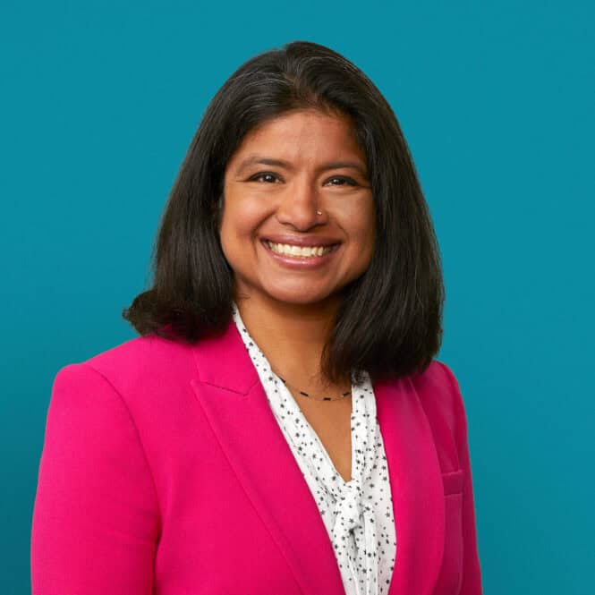 Professional headshot of Dr. Heena Santry in bright pink blazer against teal background