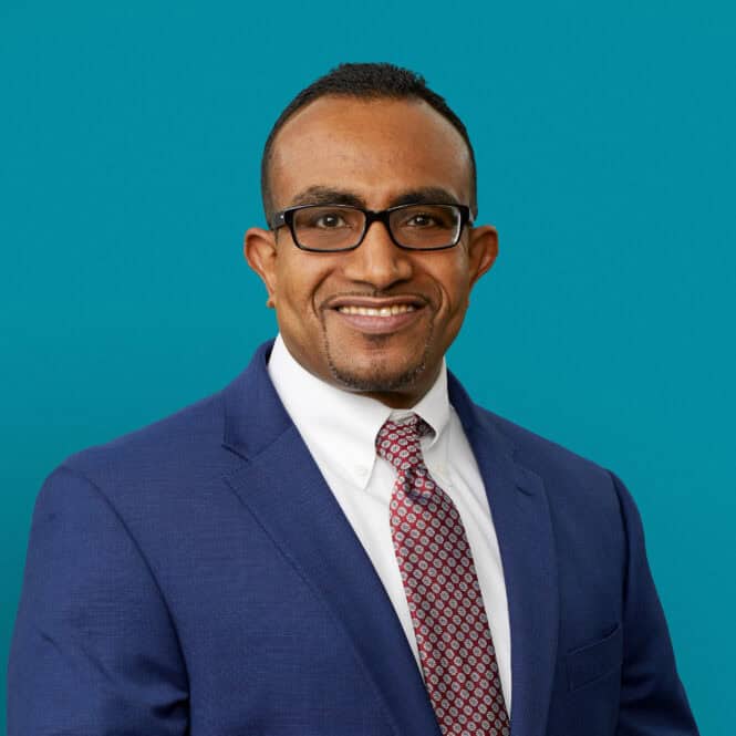 Professional headshot of Dr. Ihab Elhassan in navy suit against teal background