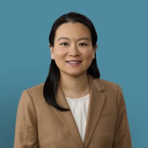 Professional headshot of Dr. Jing Li Huang in tan blazer against blue background