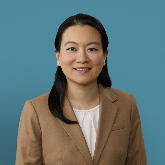 Professional headshot of Dr. Jing Li Huang in tan blazer against blue background
