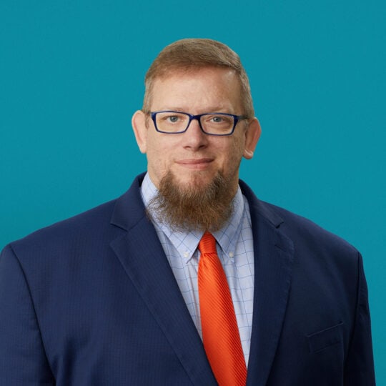Professional headshot of John Allen, PA-C in navy suit with orange tie