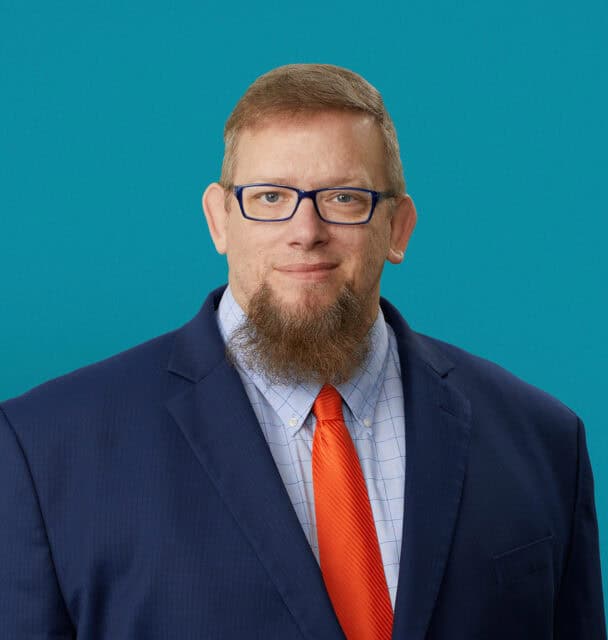 Professional headshot of John Allen, PA-C in navy suit with orange tie