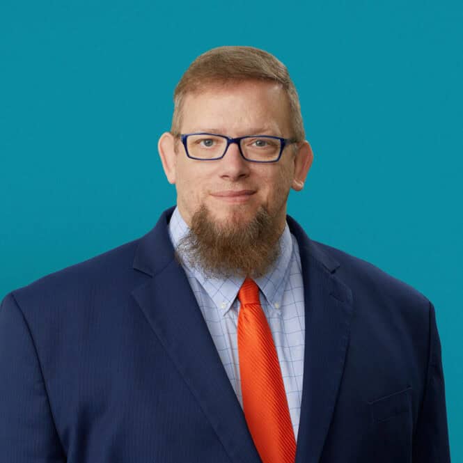 Professional headshot of John Allen, PA-C in navy suit with orange tie