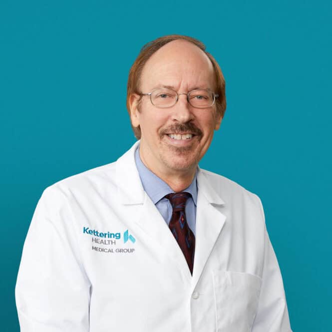 Professional headshot of John R. Bullmaster, MD in white coat against teal background
