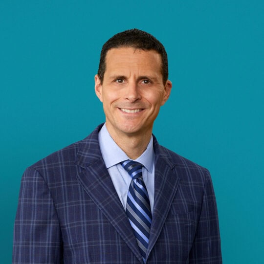 Professional headshot of John W. Sawvel, DO in navy checkered suit with striped tie