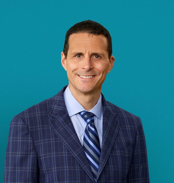 Professional headshot of John W. Sawvel, DO in navy checkered suit with striped tie