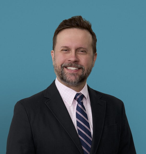Professional headshot of Dr. Jonathan Toot smiling in dark suit and striped tie