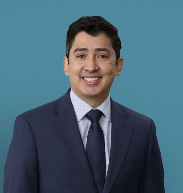 Professional headshot of Juan Linares, MD smiling in navy suit against teal background