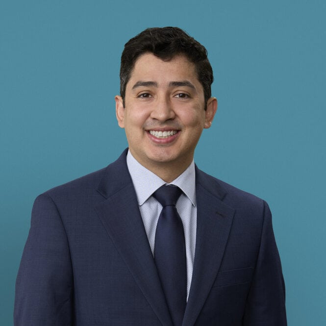 Professional headshot of Juan Linares, MD smiling in navy suit against teal background