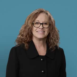 Professional headshot of Juanita Krisher, APRN-CNP, smiling woman with glasses and curly hair
