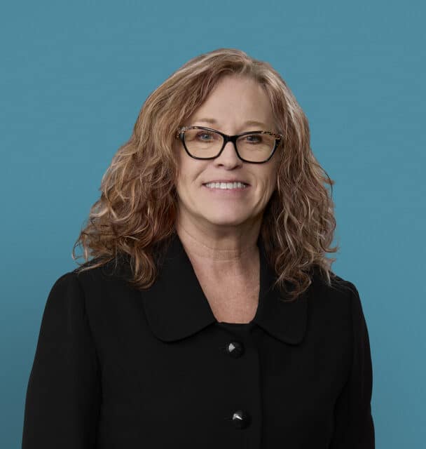 Professional headshot of Juanita Krisher, APRN-CNP, smiling woman with glasses and curly hair
