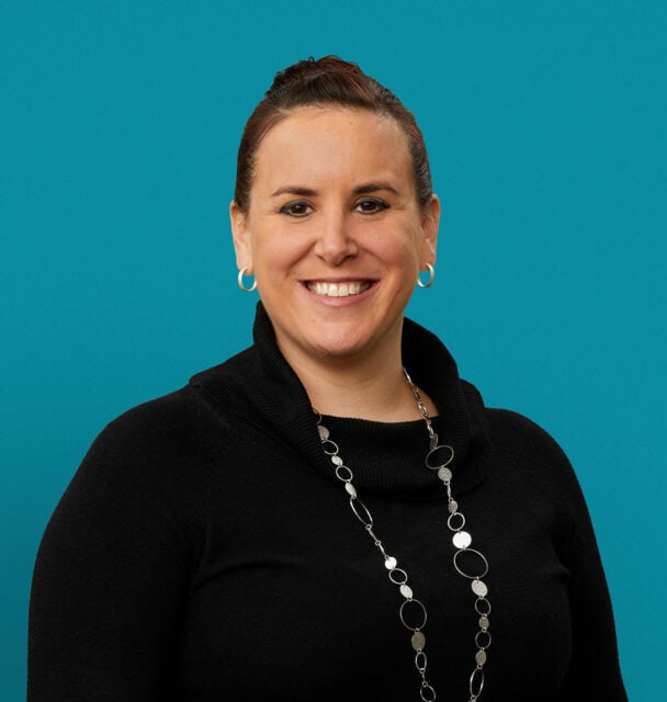 Professional headshot of Justine P. Holthaus, APRN-CNP, smiling in black attire against teal background.