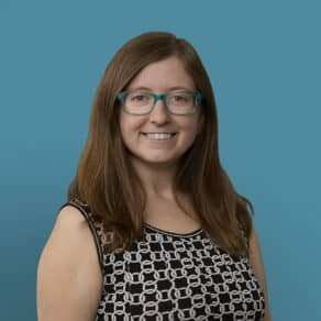 Professional headshot of Kate Meizlish, MD smiling in black patterned top with teal glasses