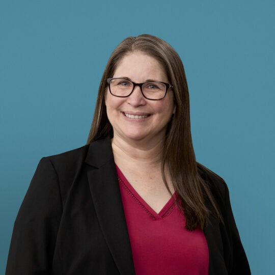 Professional headshot of Kathleen Fuchs wearing glasses, black blazer and red top