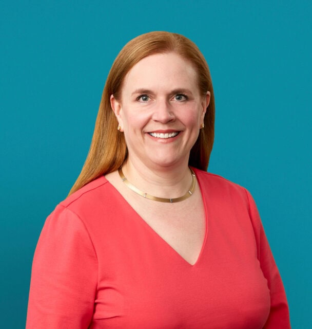 Professional headshot of Dr. Kathleen J. Oxner in coral top against teal background