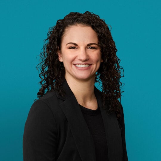 Professional headshot of Kayli D. Johnson, APRN-CNP, smiling in dark blazer against teal background.