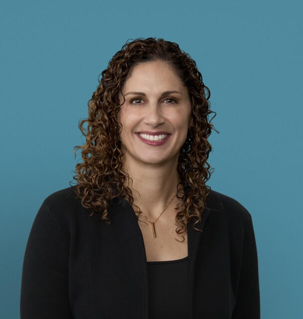 Professional headshot of Kelly Nagy, MD smiling in black blazer against blue background