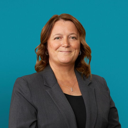 Professional headshot of Krista Miller, APRN-CNP in gray blazer against teal background