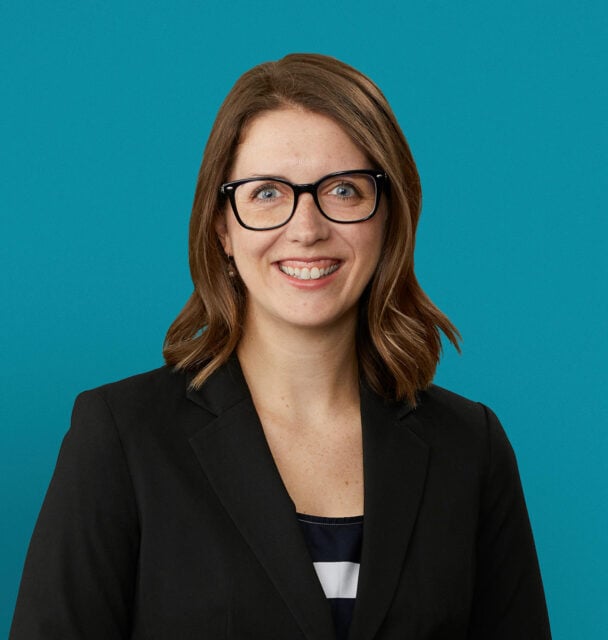 Professional headshot of Dr. Kristen Young smiling in black blazer against teal background