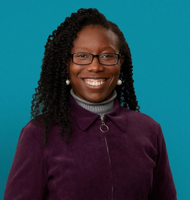 Professional headshot of Dr. Kuwong Mwamukonda smiling in purple jacket against teal background