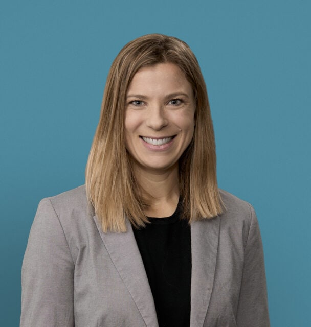 Professional headshot of Laura Adam, MD smiling in gray blazer against blue background