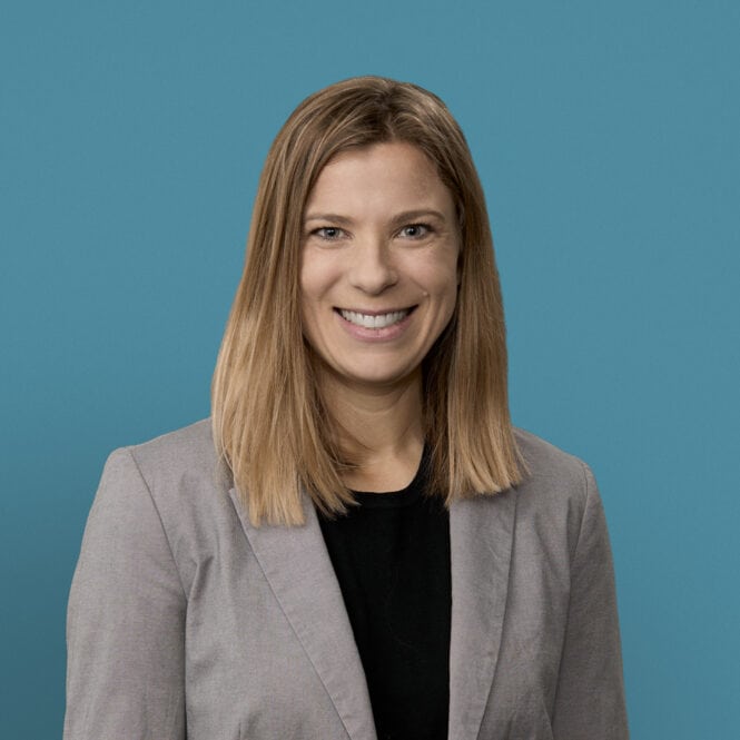Professional headshot of Laura Adam, MD smiling in gray blazer against blue background