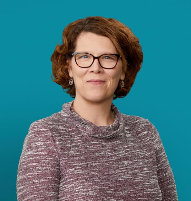 Professional headshot of Laura Knisley, APRN-CNP wearing glasses and marled sweater against teal background
