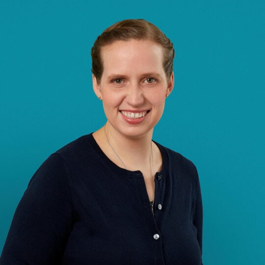 Professional headshot of Dr. Lindsey M. Miller in navy cardigan against teal background