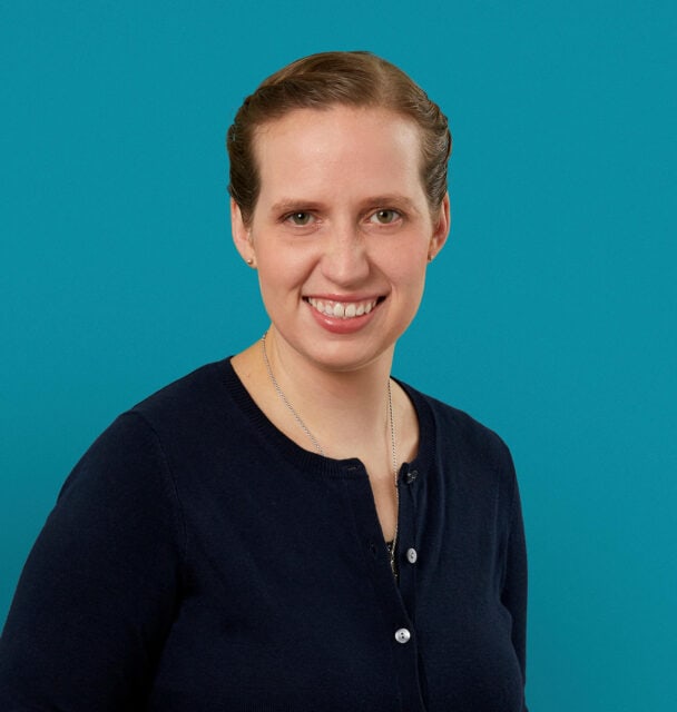 Professional headshot of Dr. Lindsey M. Miller in navy cardigan against teal background