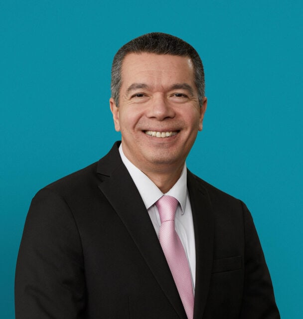 Professional headshot of Luis Perez, DO in dark suit with pink tie