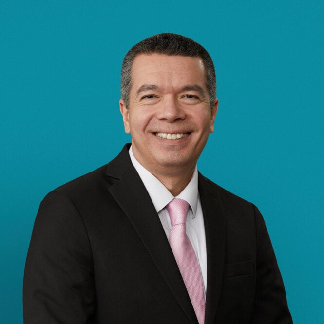 Professional headshot of Luis Perez, DO in dark suit with pink tie