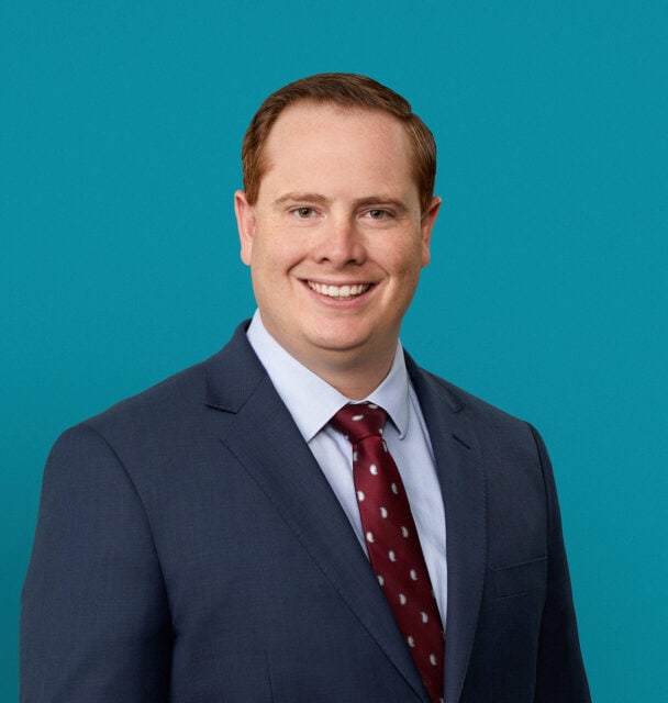 Professional headshot of Dr. Luke M. Lewis in navy suit with red tie