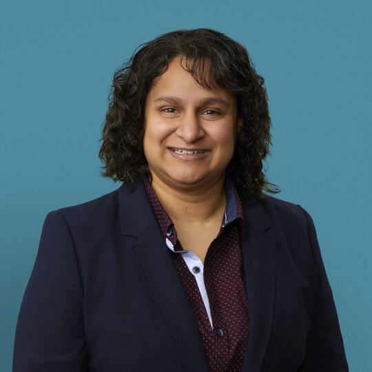 Professional headshot of Dr. Manisha Patel in dark blazer against blue background