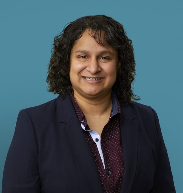 Professional headshot of Dr. Manisha Patel in dark blazer against blue background