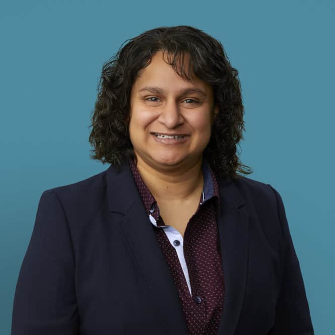 Professional headshot of Dr. Manisha Patel in dark blazer against blue background