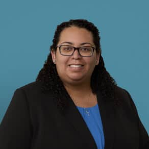 Professional headshot of Dr. Mara Bryan wearing glasses and dark blazer with blue shirt.