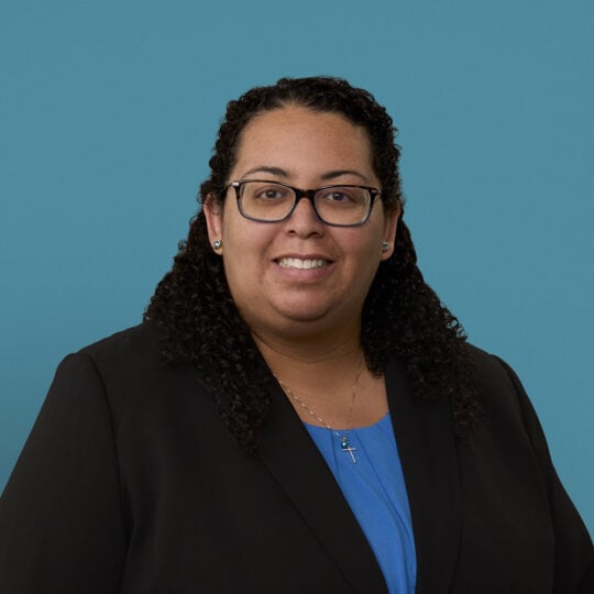 Professional headshot of Dr. Mara Bryan wearing glasses and dark blazer with blue shirt.