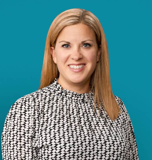 Professional headshot of Melanie Johnson, APRN-CNP, smiling in patterned blouse against teal background.